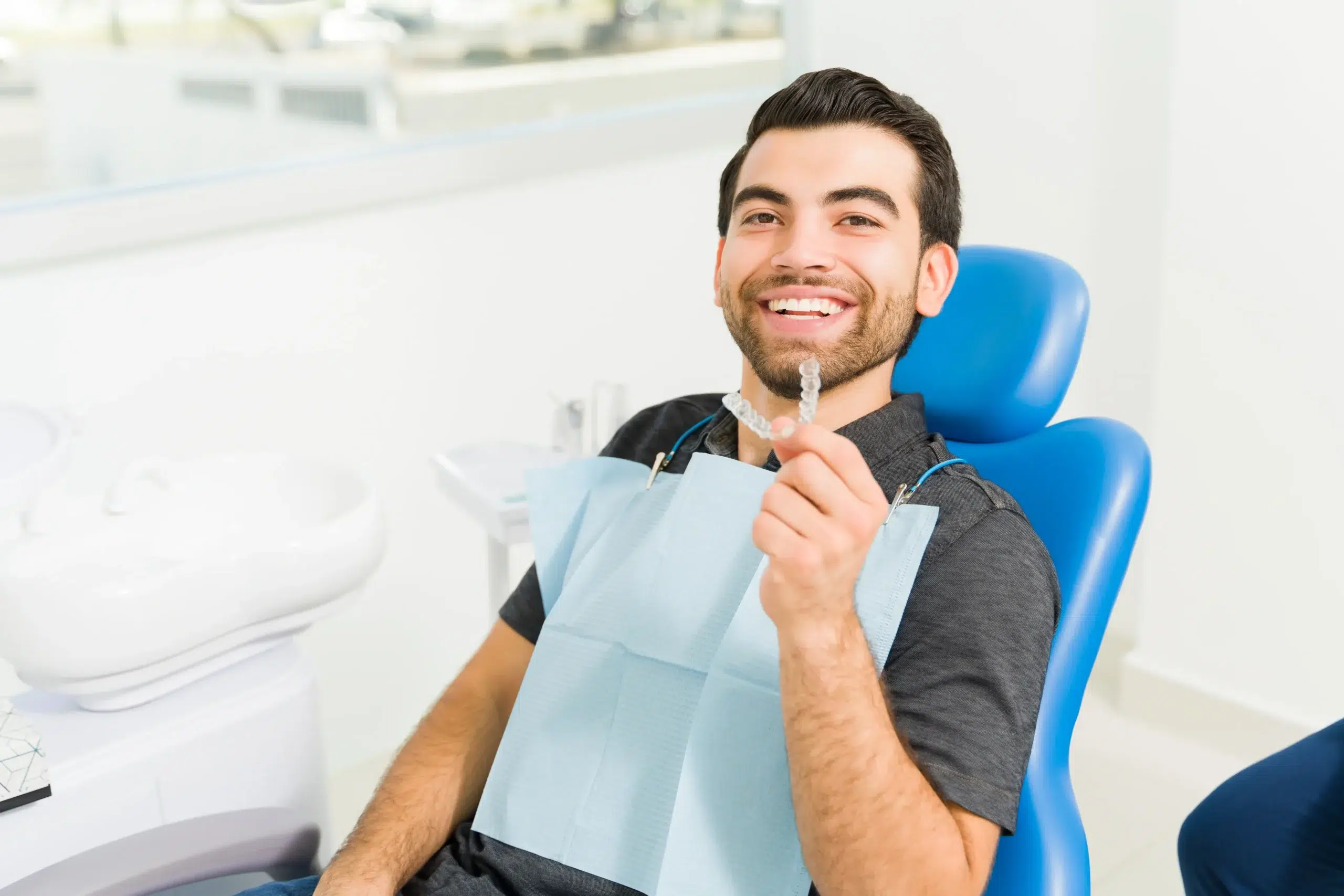 Man holding dental model in dental office chair, smiling at camera