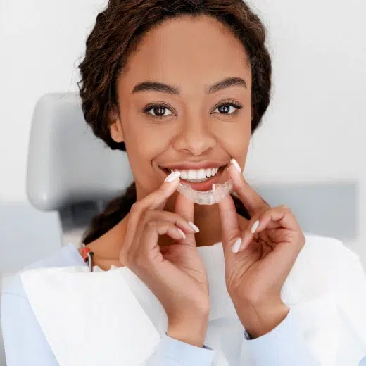 Young woman holding clear aligner trays, smiling at camera against white background.